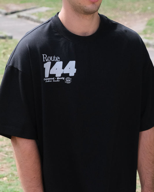 Man wearing a black t-shirt with 'Route 144' text standing outdoors.