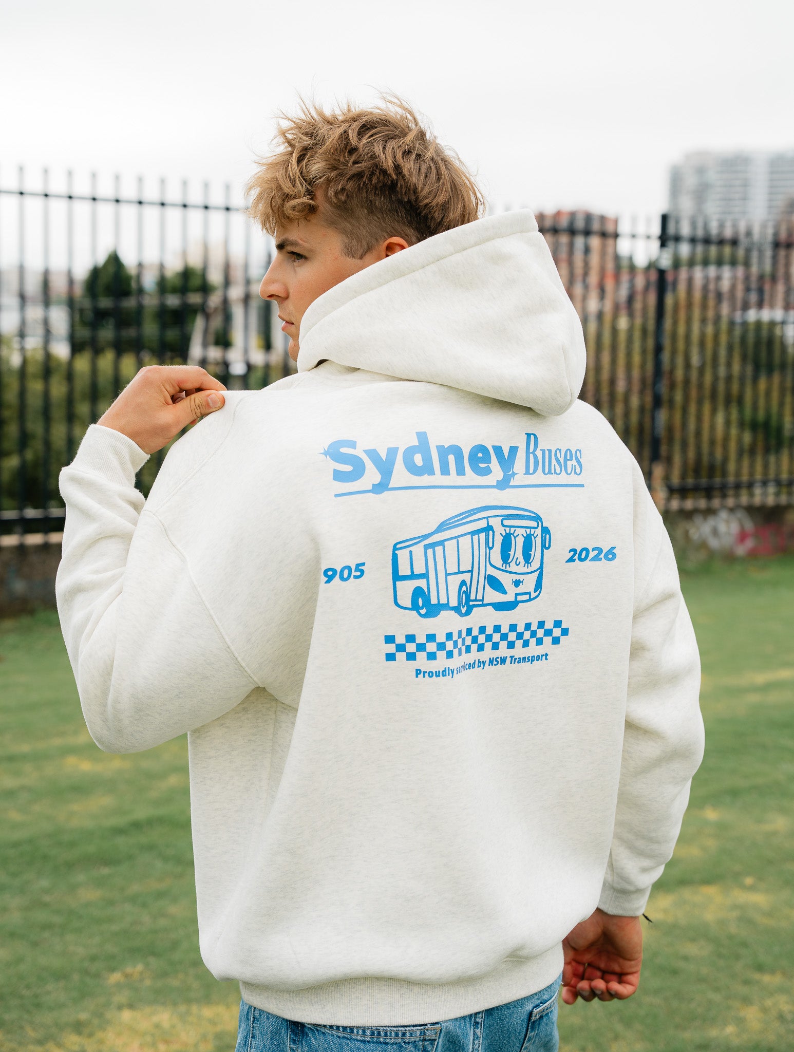 Person wearing a white hoodie with 'Sydney Buses' branding on the back, standing outdoors.