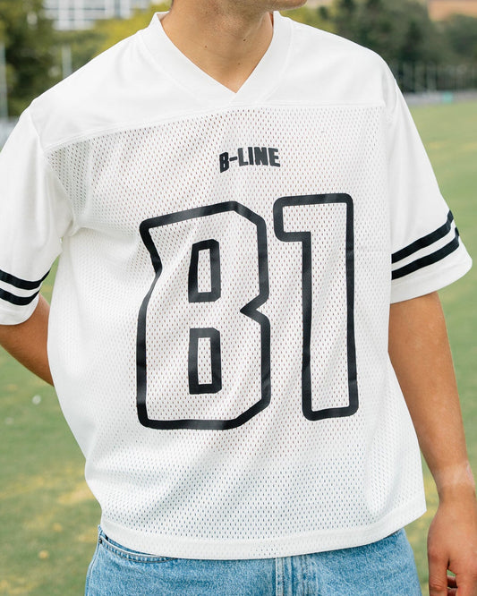 Person wearing a white B-Line sports jersey with black lettering on a grassy field.