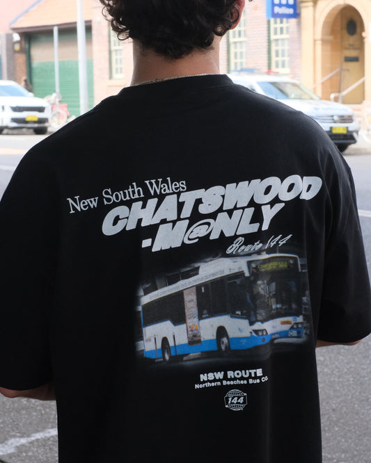 Person wearing a black t-shirt with text and graphics on the back, standing on a street.