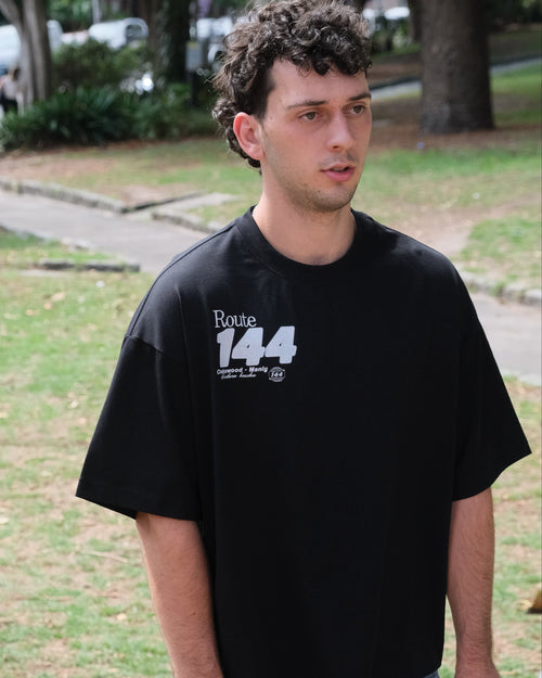 Man wearing a black t-shirt with 'Route 144' text standing outdoors.